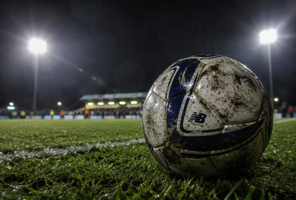 Wet football on turf under floodlights